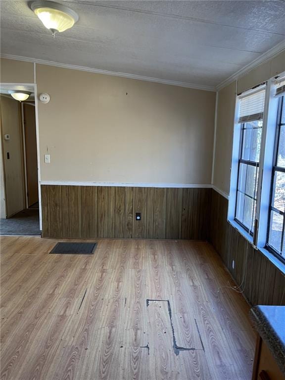 unfurnished room featuring wooden walls, ornamental molding, a textured ceiling, and light wood-type flooring