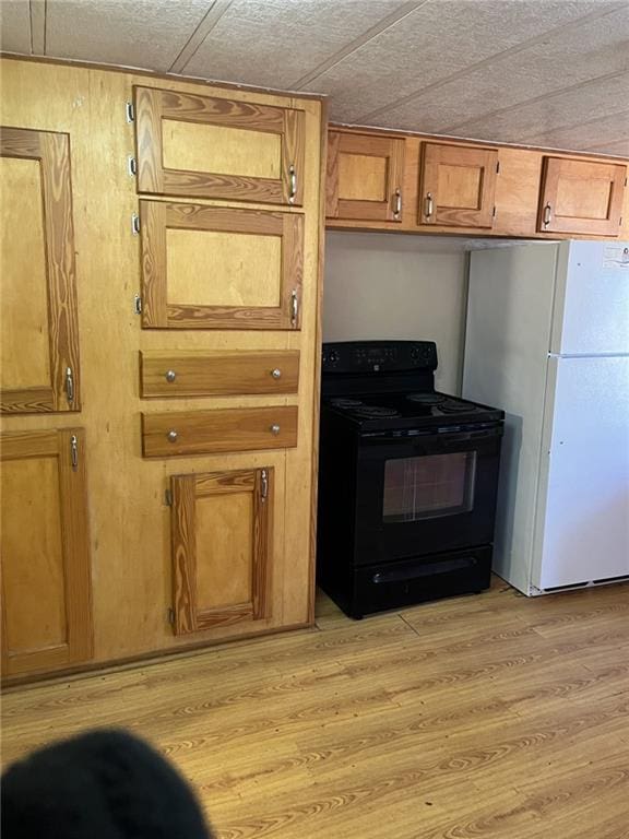 kitchen featuring black electric range oven, light hardwood / wood-style flooring, a wood stove, and white refrigerator