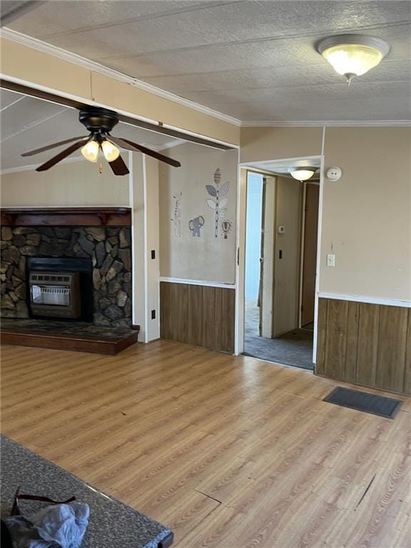 unfurnished living room featuring ornamental molding, a stone fireplace, wooden walls, and light wood-type flooring