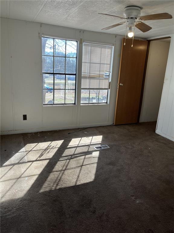 spare room featuring ceiling fan, dark carpet, and a textured ceiling