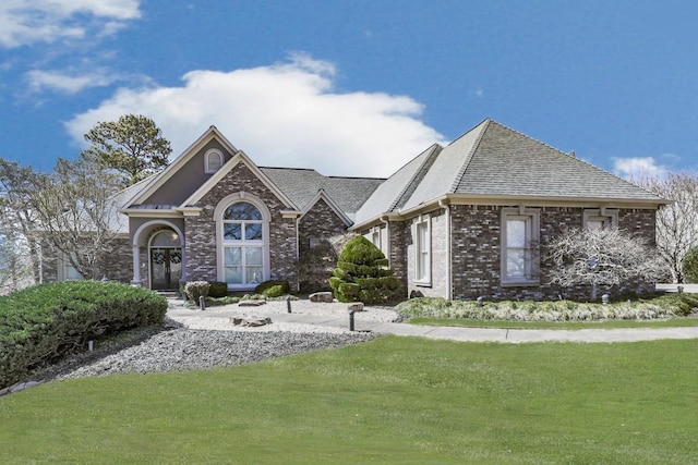 view of front of house featuring a front lawn, brick siding, and roof with shingles