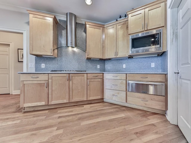 kitchen with stainless steel microwave, light brown cabinets, a warming drawer, and wall chimney range hood