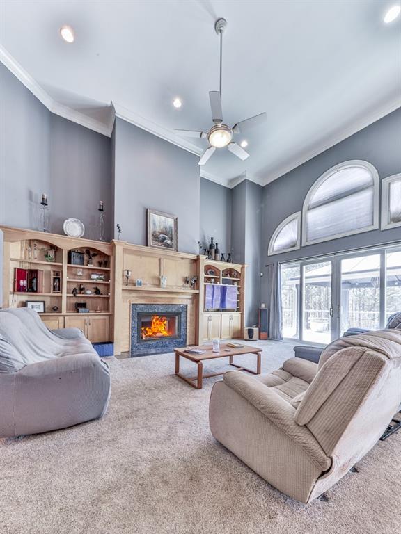 carpeted living area featuring crown molding, a warm lit fireplace, and ceiling fan