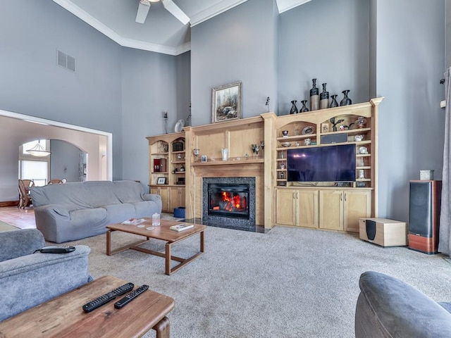 living room featuring visible vents, a fireplace with flush hearth, arched walkways, ornamental molding, and a towering ceiling