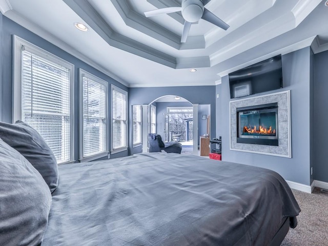 carpeted bedroom featuring a tray ceiling, multiple windows, and ornamental molding