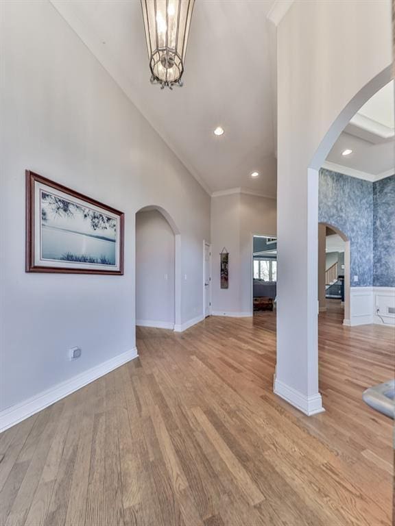 unfurnished living room featuring a wainscoted wall, arched walkways, light wood finished floors, and a chandelier