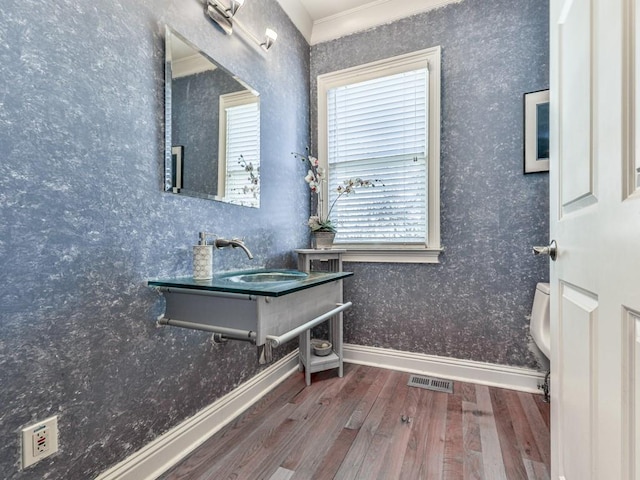 bathroom with wood finished floors, visible vents, baseboards, wallpapered walls, and a sink