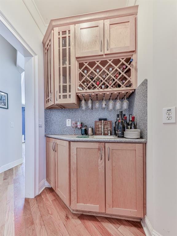 bar featuring a bar, light wood-style flooring, baseboards, and backsplash