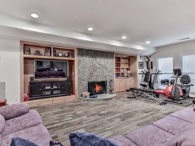 exercise room featuring visible vents, built in features, recessed lighting, a fireplace, and wood finished floors