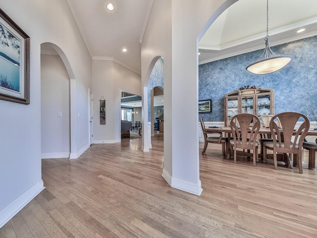 foyer entrance featuring light wood-style flooring, arched walkways, crown molding, wallpapered walls, and baseboards