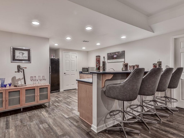 kitchen with visible vents, recessed lighting, freestanding refrigerator, dark wood-type flooring, and a kitchen breakfast bar