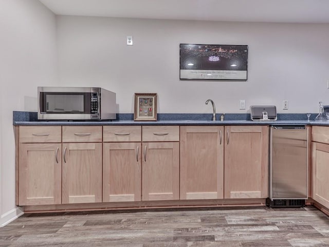 bar with stainless steel microwave, light wood-type flooring, and a sink