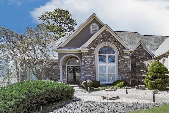 traditional-style home with a standing seam roof, french doors, a shingled roof, metal roof, and brick siding