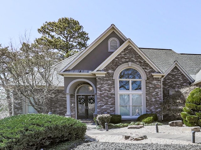 traditional-style house featuring french doors, brick siding, and roof with shingles