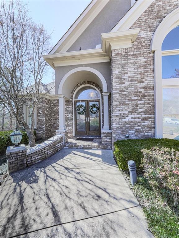 property entrance featuring french doors, brick siding, and stucco siding