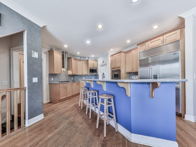 kitchen with light wood-style flooring, light brown cabinetry, built in appliances, a kitchen breakfast bar, and backsplash