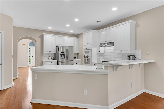 1712 Bonnabel Trce NE, Marietta, GA 30066 - kitchen featuring stainless steel fridge with ice dispenser, under cabinet range hood, white double oven, a peninsula, and arched walkways