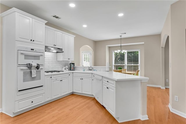 1712 Bonnabel Trce NE, Marietta, GA 30066 - kitchen featuring arched walkways, a peninsula, white appliances, light wood-type flooring, and under cabinet range hood