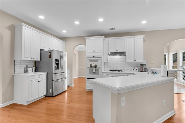 1712 Bonnabel Trce NE, Marietta, GA 30066 - kitchen with stainless steel fridge with ice dispenser, arched walkways, white double oven, under cabinet range hood, and decorative backsplash