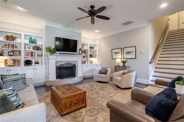 living room featuring crown molding, a fireplace, built in shelves, and ceiling fan