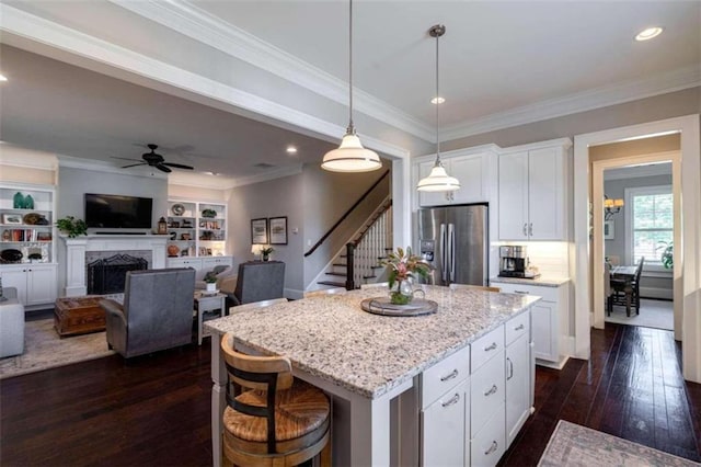 kitchen with white cabinetry, light stone counters, stainless steel fridge with ice dispenser, hanging light fixtures, and a kitchen island