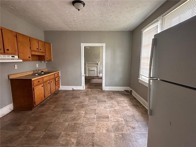 6 Hazel St, Porterdale, GA 30014 - kitchen with freestanding refrigerator, under cabinet range hood, a textured ceiling, brown cabinets, and light countertops