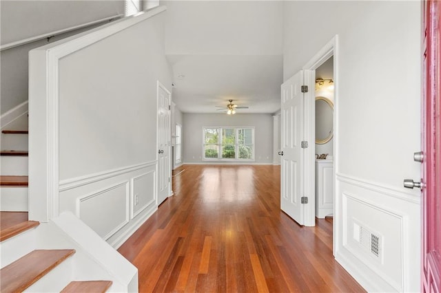 hallway featuring visible vents, stairs, wainscoting, wood finished floors, and a decorative wall