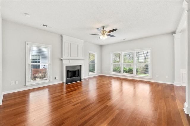 unfurnished living room with visible vents, a textured ceiling, wood finished floors, a fireplace, and ceiling fan