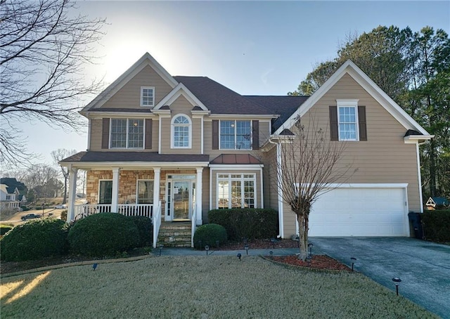 view of front of property featuring covered porch, a garage, driveway, stone siding, and a front yard