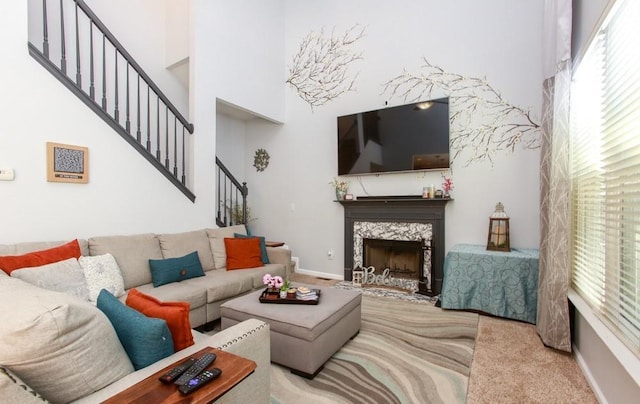 carpeted living room with a towering ceiling, stairway, a high end fireplace, and baseboards
