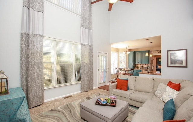living room featuring carpet flooring, visible vents, baseboards, a towering ceiling, and ceiling fan with notable chandelier
