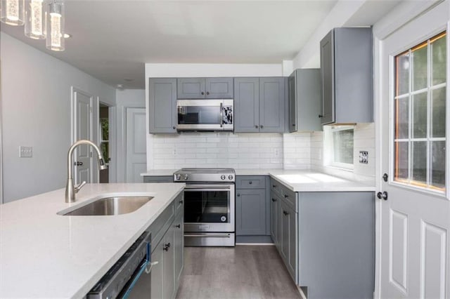 kitchen featuring dark wood-type flooring, gray cabinetry, sink, pendant lighting, and appliances with stainless steel finishes