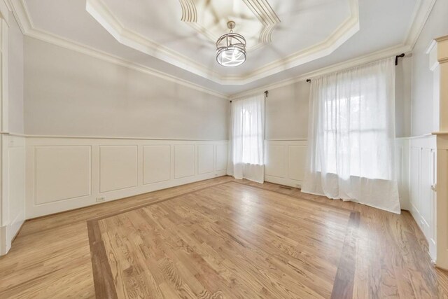 empty room featuring a notable chandelier, light hardwood / wood-style floors, a raised ceiling, and ornamental molding