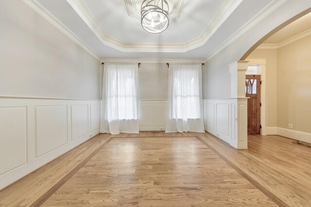 spare room featuring a tray ceiling, crown molding, and light wood-type flooring