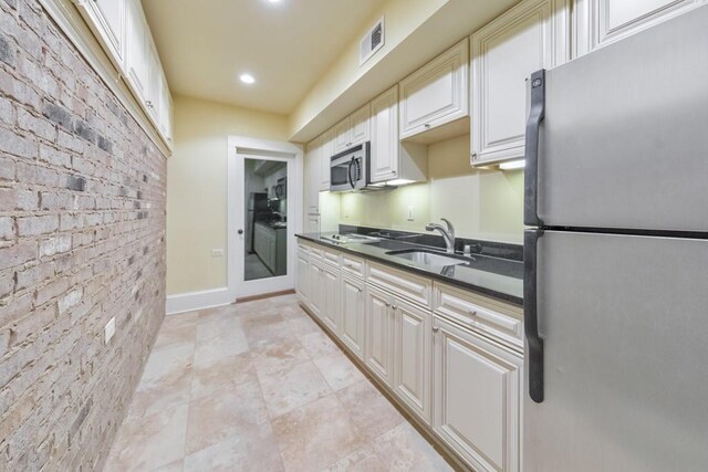 kitchen with brick wall, white cabinetry, sink, and appliances with stainless steel finishes