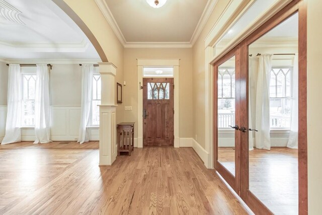 foyer entrance featuring light wood-type flooring, crown molding, and a healthy amount of sunlight