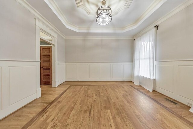 unfurnished room featuring a tray ceiling, crown molding, light hardwood / wood-style flooring, and an inviting chandelier