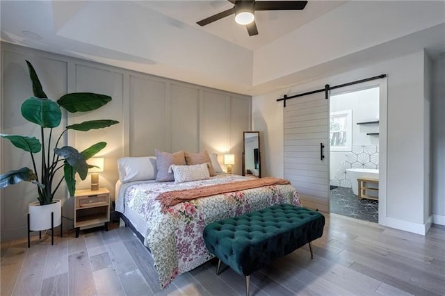 bedroom with hardwood / wood-style flooring, ceiling fan, a barn door, and a tray ceiling