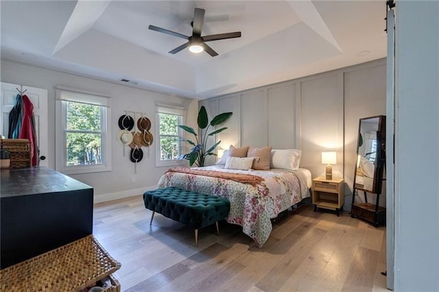 bedroom featuring ceiling fan, a raised ceiling, and light wood-type flooring