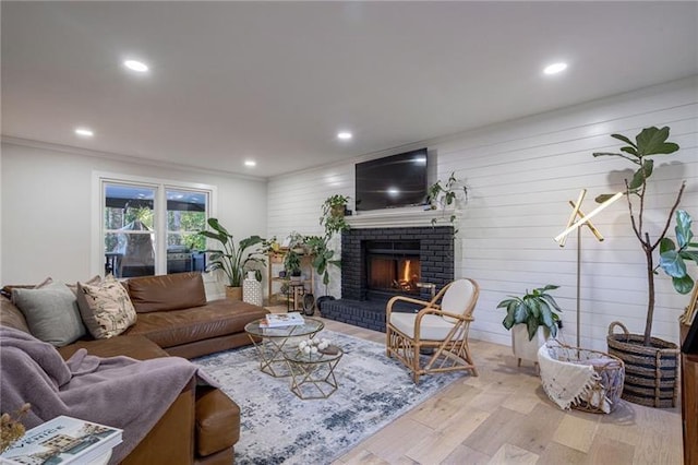 living room featuring wooden walls, ornamental molding, light wood-type flooring, and a brick fireplace