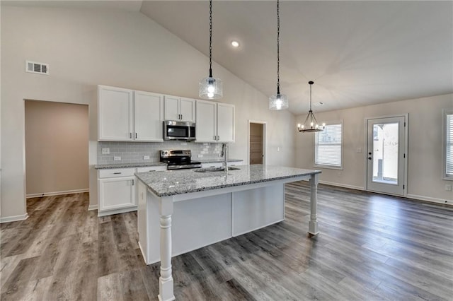 kitchen with white cabinetry, appliances with stainless steel finishes, an island with sink, and light stone counters