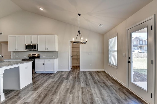 kitchen featuring vaulted ceiling, appliances with stainless steel finishes, white cabinets, hanging light fixtures, and light stone countertops