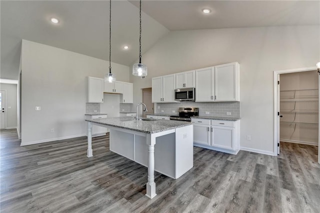 kitchen with a center island with sink, stainless steel appliances, light stone countertops, white cabinets, and a kitchen bar