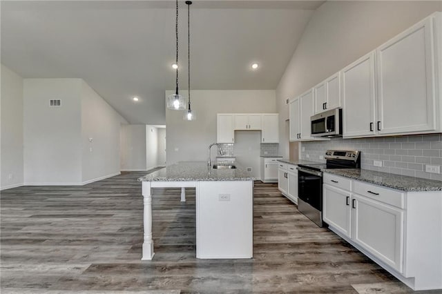 kitchen with white cabinetry, hanging light fixtures, dark stone counters, stainless steel appliances, and a kitchen island with sink