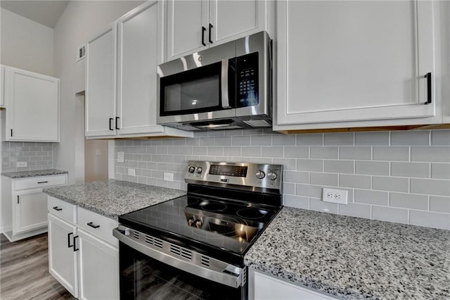 kitchen featuring stainless steel appliances, light stone countertops, white cabinets, and backsplash