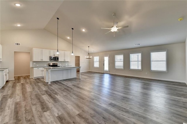 kitchen featuring appliances with stainless steel finishes, a kitchen island with sink, hanging light fixtures, white cabinets, and a kitchen bar