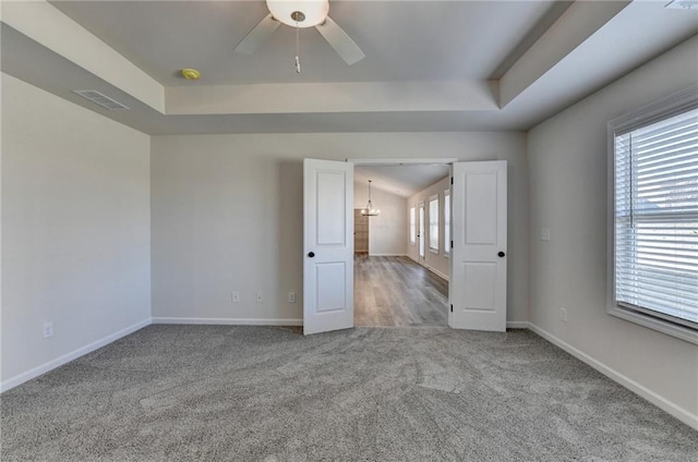 unfurnished room with a healthy amount of sunlight, carpet flooring, ceiling fan, and a tray ceiling