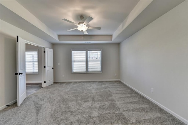 carpeted empty room with a tray ceiling, a wealth of natural light, and ceiling fan