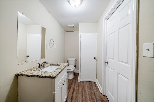 half bathroom featuring toilet, wood finished floors, vanity, and baseboards