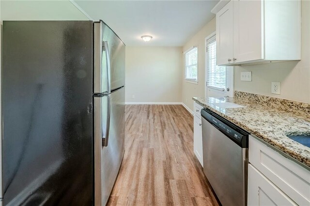 kitchen with baseboards, light stone countertops, stainless steel appliances, white cabinetry, and light wood-type flooring